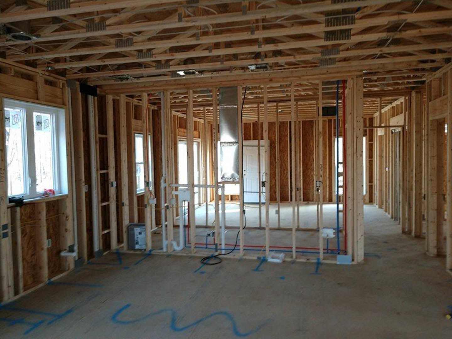 Unfinished room with exposed wood framing, ceiling beams, blue tape marking surfaces, and a window displaying taped notes