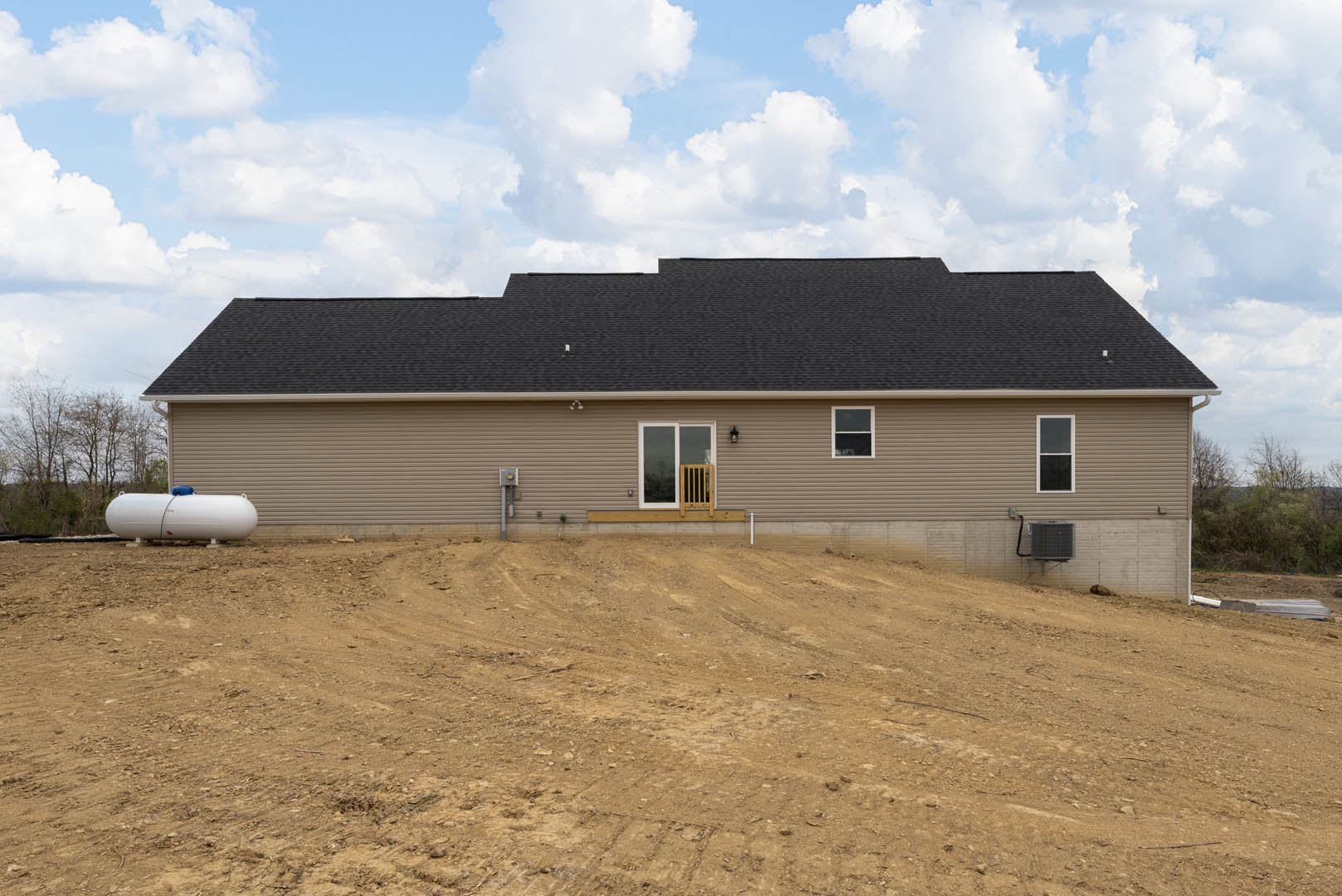 Modern cottage-style house with light exterior siding, single door and window, wooden railing, dirt hill in foreground, retaining wall, white water tank with blue top, and outdoor