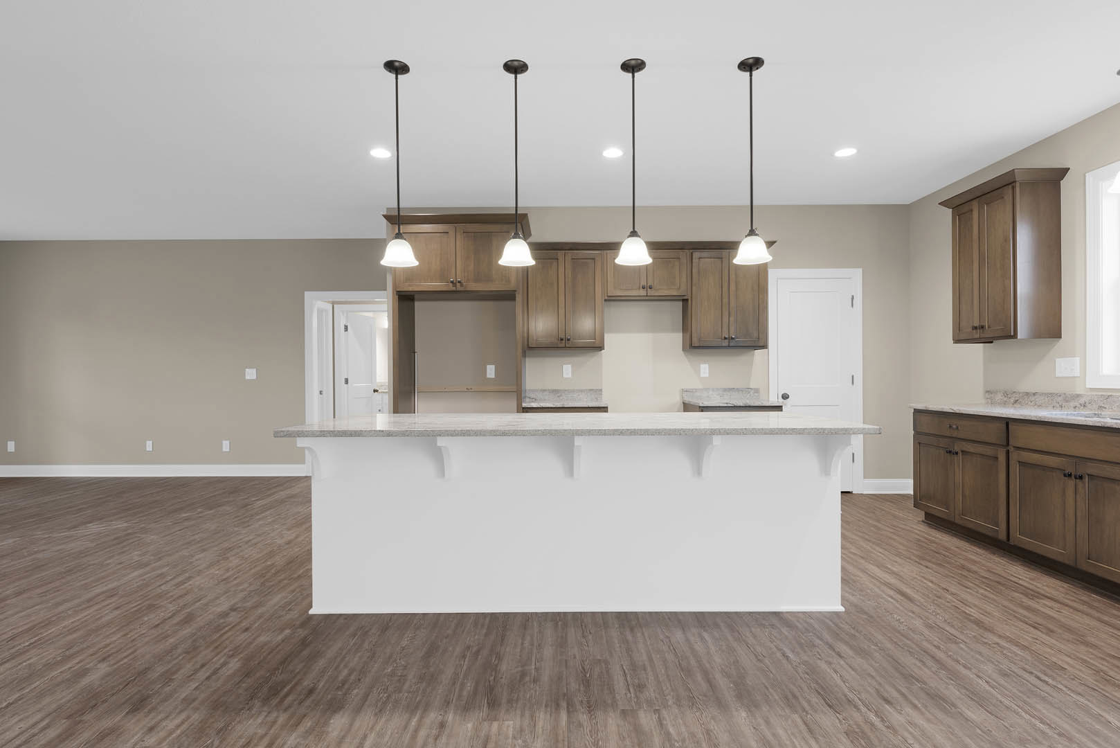 Open kitchen with white countertop bar, wood flooring, white cabinetry with silver handles, and white walls