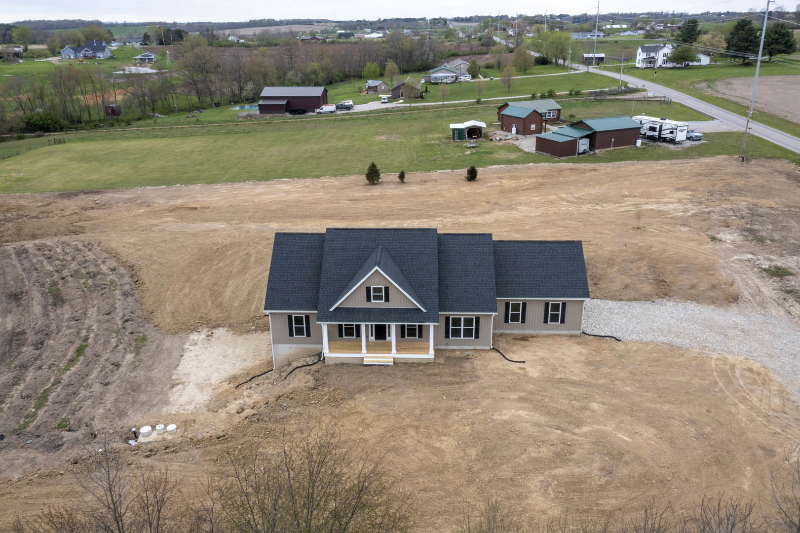 Two-story house with black roof, white siding, black front door framed by white pillars, large bare dirt patch in front yard, windows on both floors, surrounded by sparse grass and