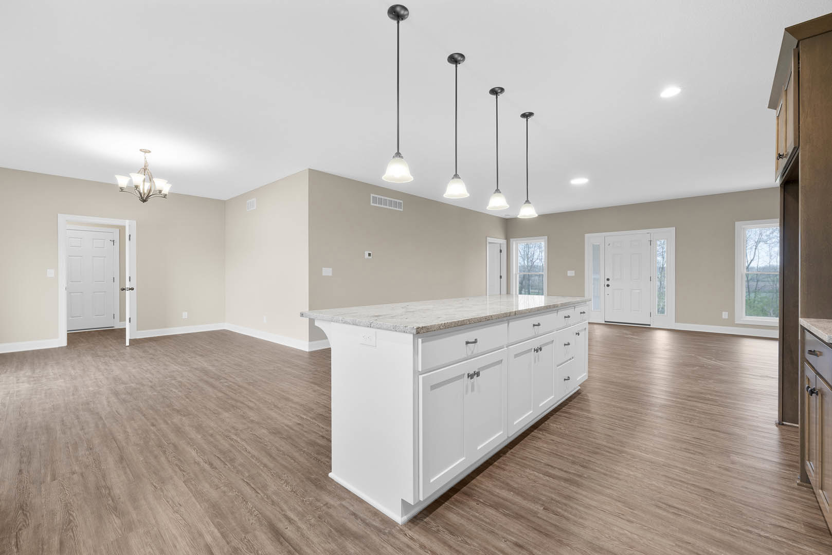 Spacious kitchen featuring a large white island with marble countertop, white cabinetry, laminate flooring, glass-paneled door, and window overlooking trees