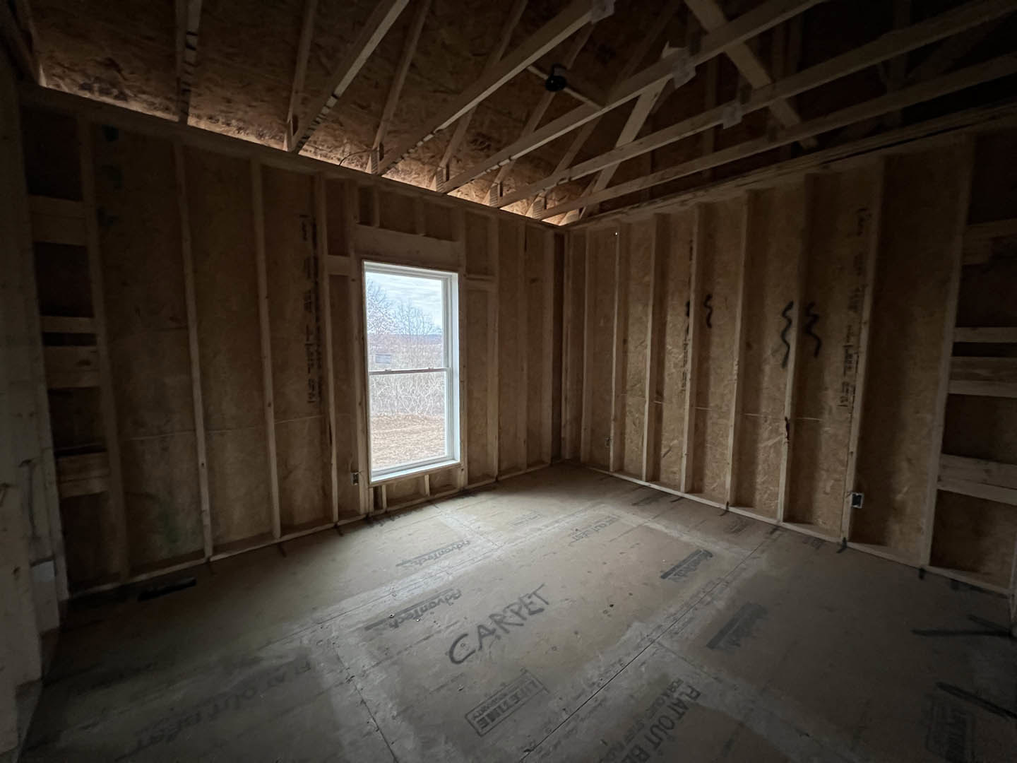 Bright room featuring exposed wood ceiling beams, large window overlooking grassy field, light plaster walls, and smooth plank flooring.