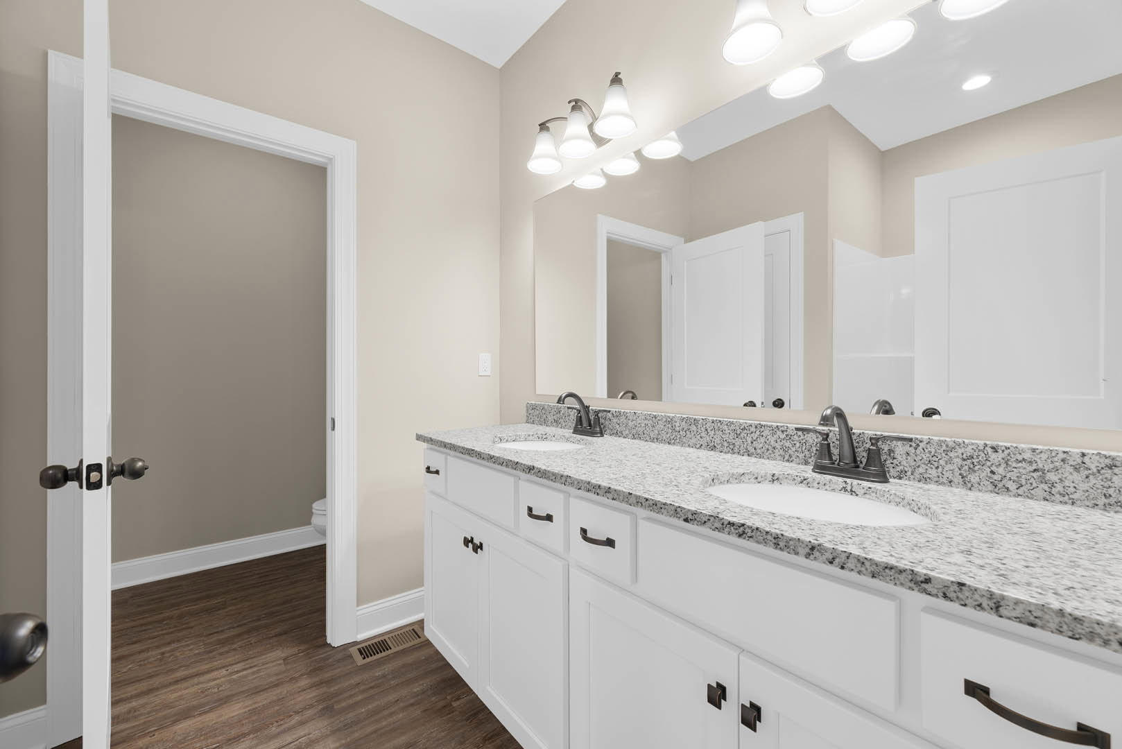 Bathroom with marble countertop, large wall mirror, white cabinetry, chrome faucet, and tiled walls; partial view of bathtub, white door, and wall vent.