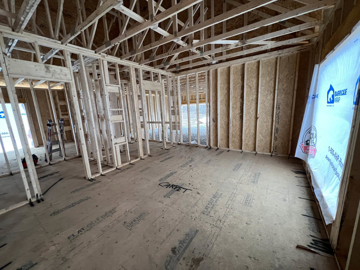Open room with exposed wood ceiling beams, unfinished walls, metal ladder leaning against wall, construction materials scattered on subfloor.