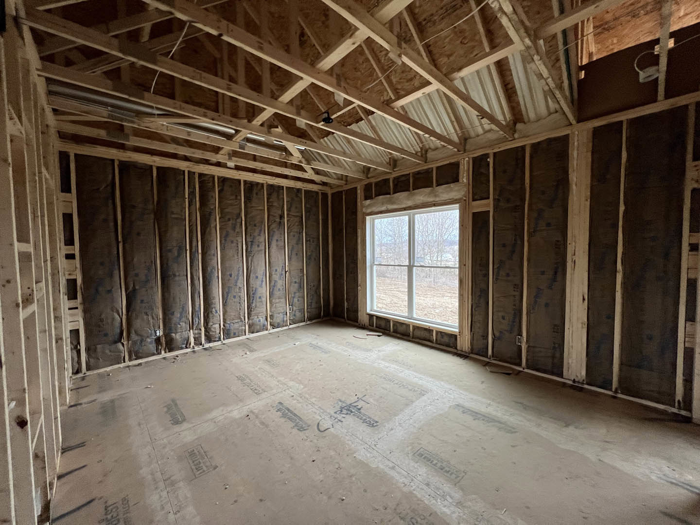 Exposed wood ceiling beams, large window with outdoor view, concrete floor, white ceiling panels, wood accent wall
