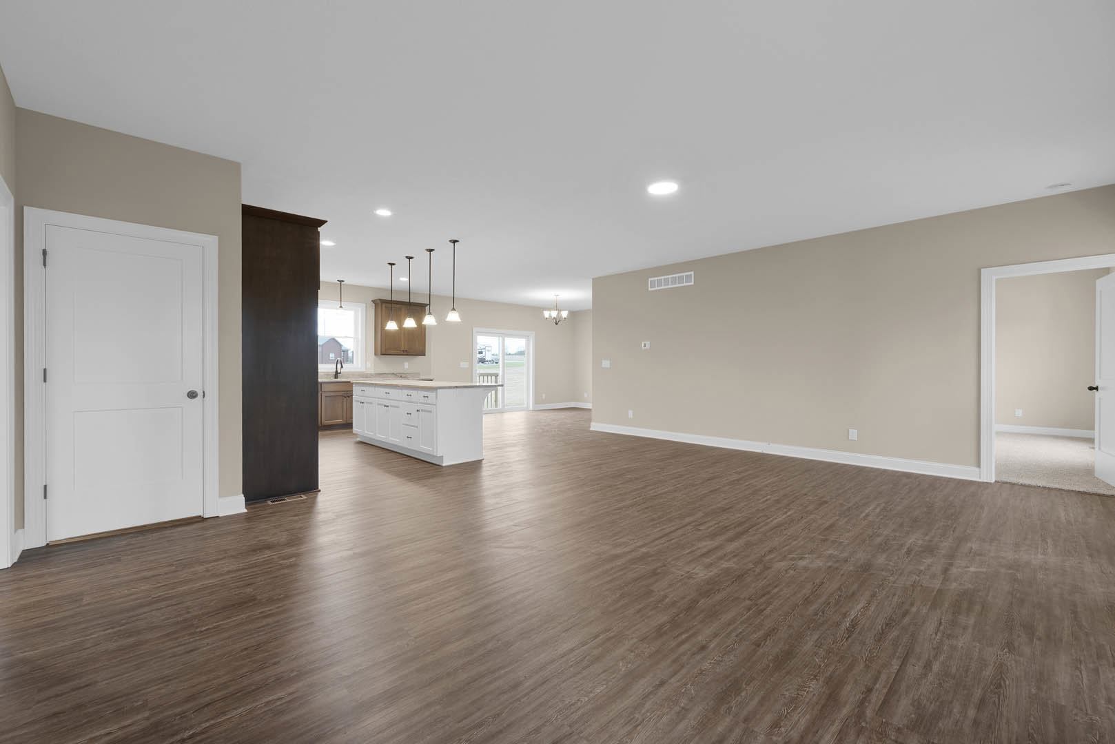 Spacious room featuring hardwood flooring, white cabinetry, white kitchen island with drawers, white walls, and a white door with silver handle