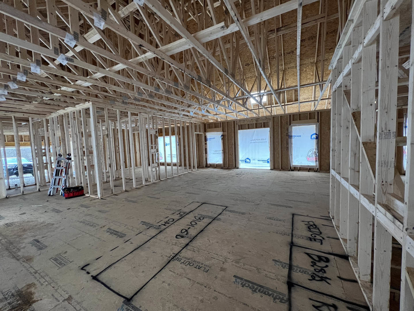 Open room with exposed ceiling beams, two metal ladders, white sign with blue and black writing, white box with blue and black logos, ladder holding a few books, red and black bag