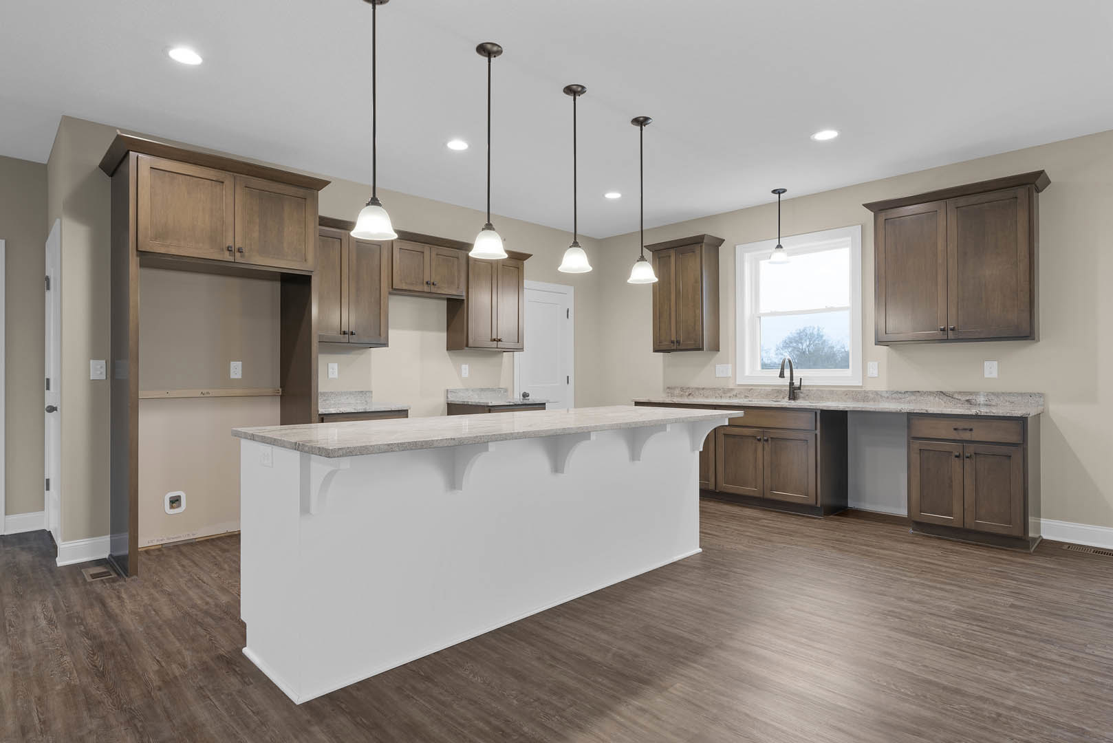 White kitchen island with waterfall countertop, dark wood cabinets, wood flooring, stainless steel sink beneath a window, black pendant light fixture, and modern appliances.