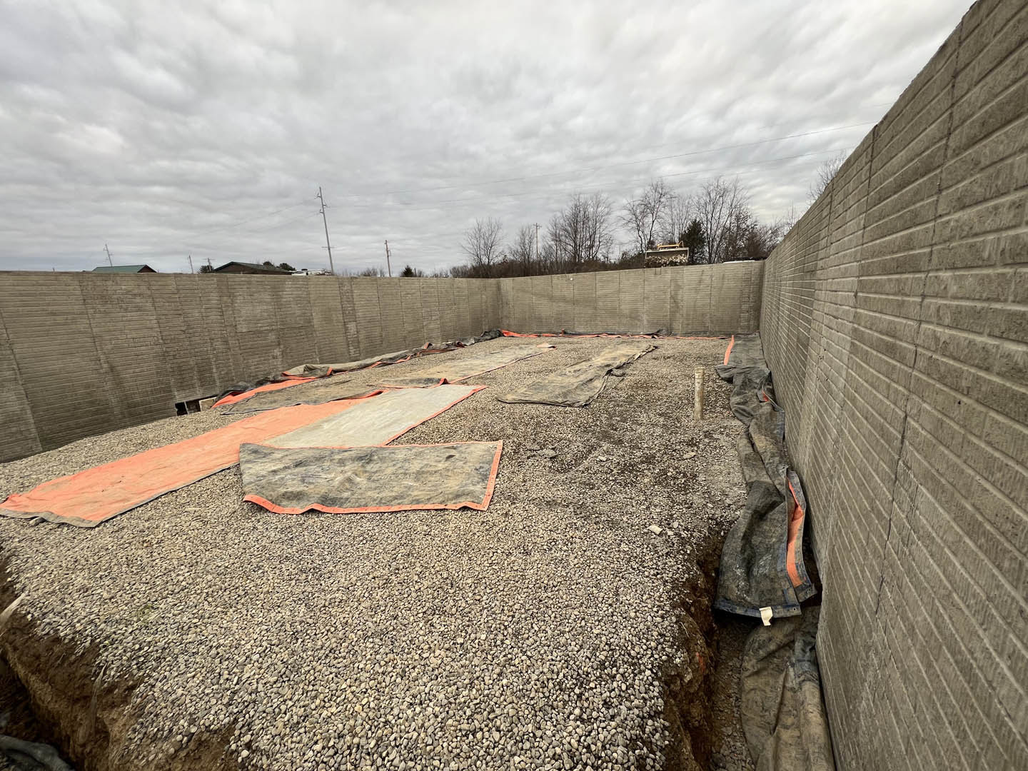 Concrete wall with scattered gravel and a pile of tarps on the ground, cloudy sky and trees in the background