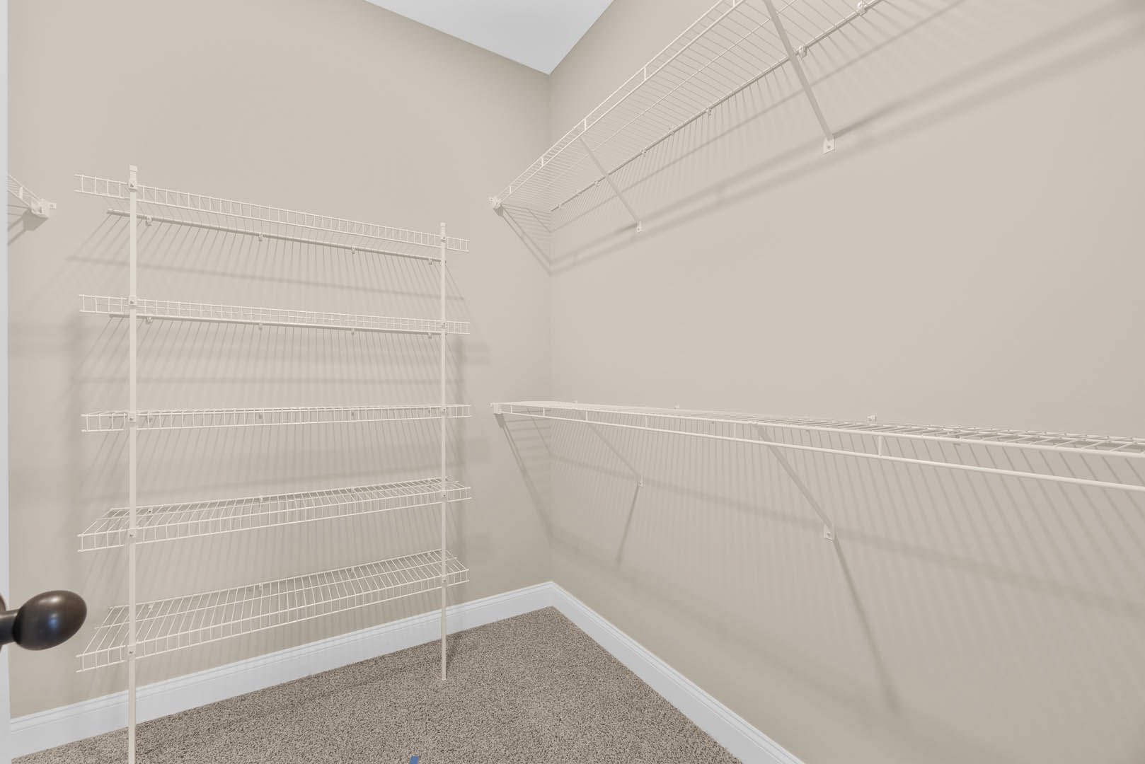 White built-in shelves mounted on a wall, blue decorative object displayed on a shelf, light carpet flooring, white wire rack visible in corner.