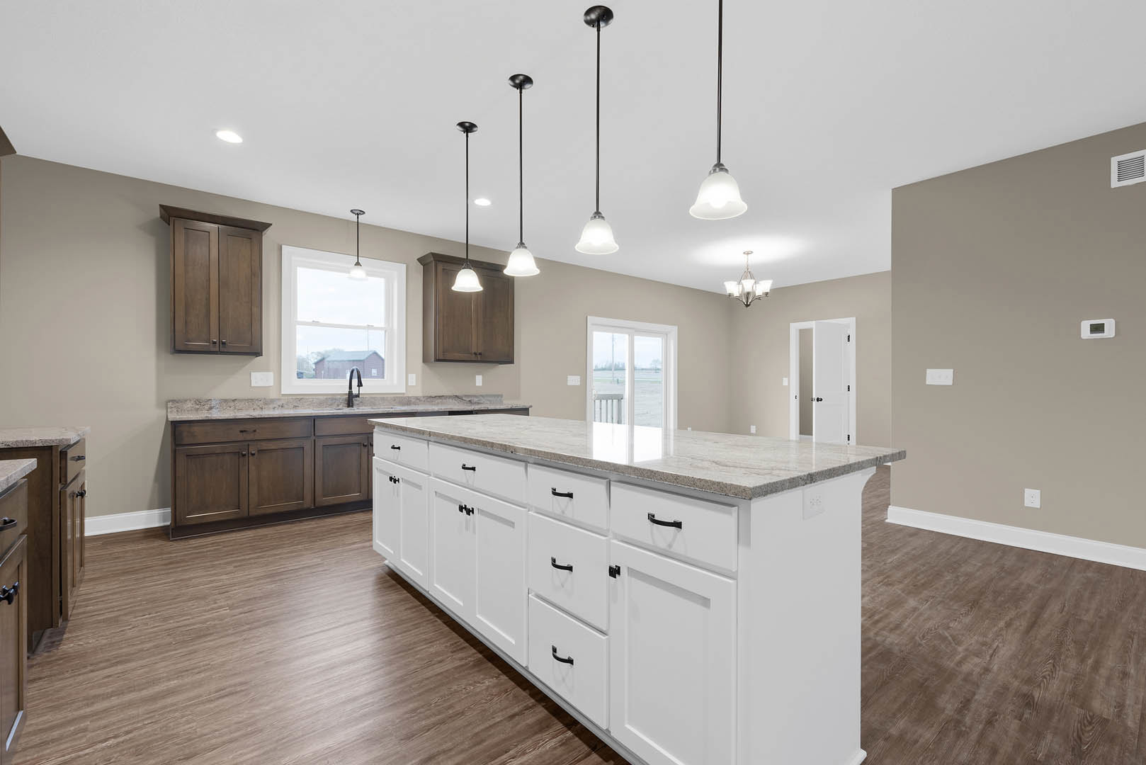 White kitchen with shaker cabinets, large central island featuring black hardware, quartz countertops, farmhouse sink, pendant lights hanging above, and glass-paneled door in the