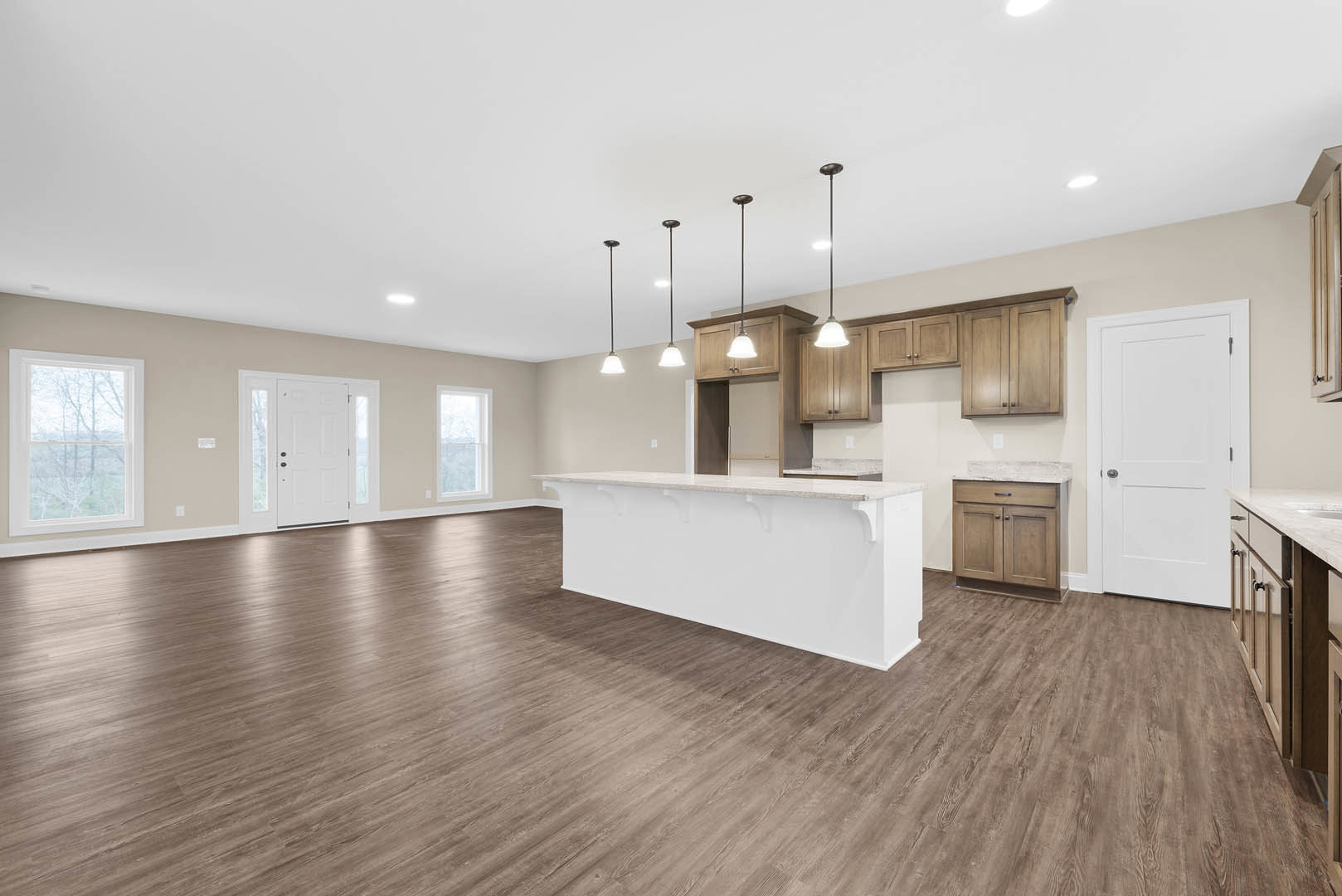 Open kitchen and living room featuring wood flooring, white countertops, white cabinetry, black door handle, large window overlooking trees, and white walls.