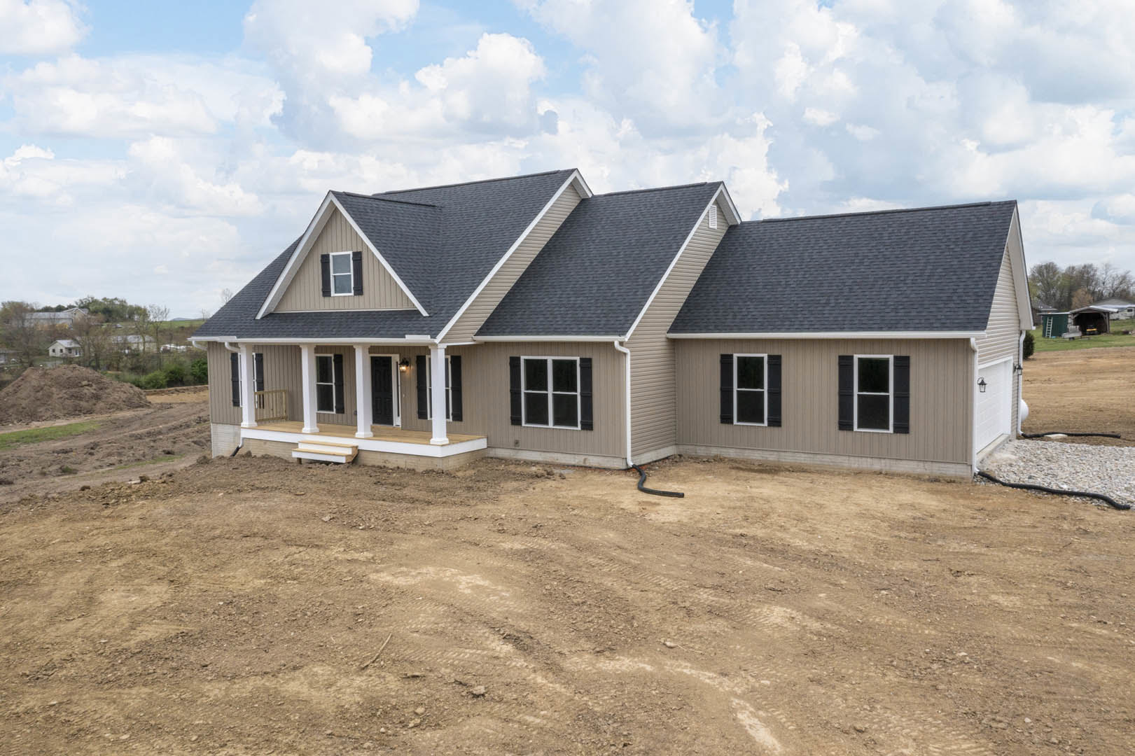 Two-story home with black-shuttered windows, light siding, and unfinished dirt yard; visible roofline and metal railing near entrance.