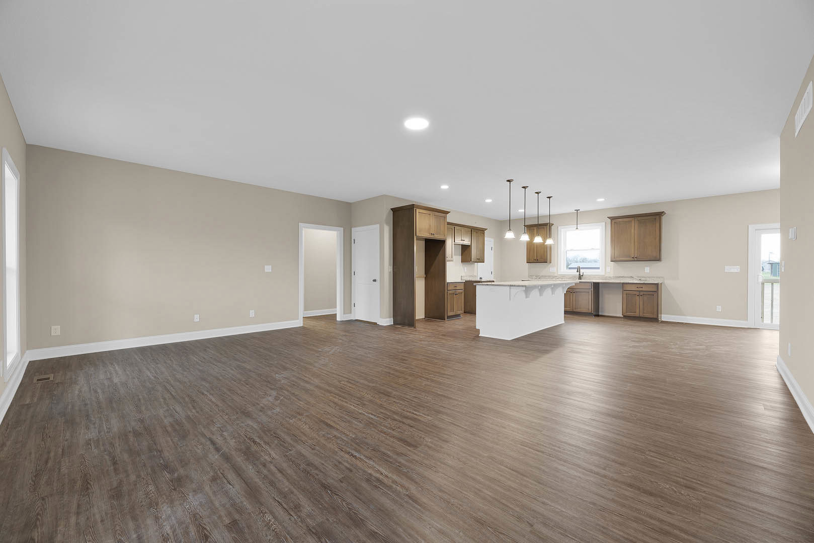 Open-concept kitchen and dining area with wood flooring, white walls, recessed ceiling lights, and wooden cabinets with metal handles