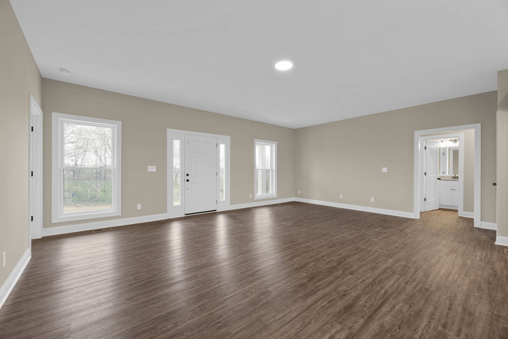 Wood flooring and white plaster walls in a bright room with recessed ceiling light, large window overlooking trees, and a white door with glass panes