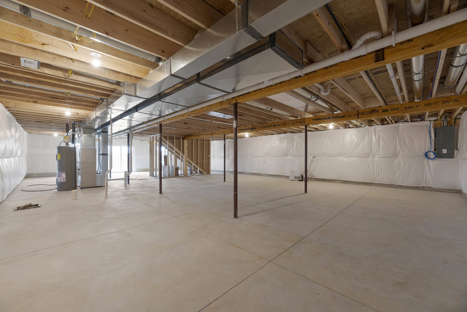 White floor with exposed wooden ceiling beams, large white wall, glass door with yellow sign, white fabric and plastic covering on wall, basement interior.