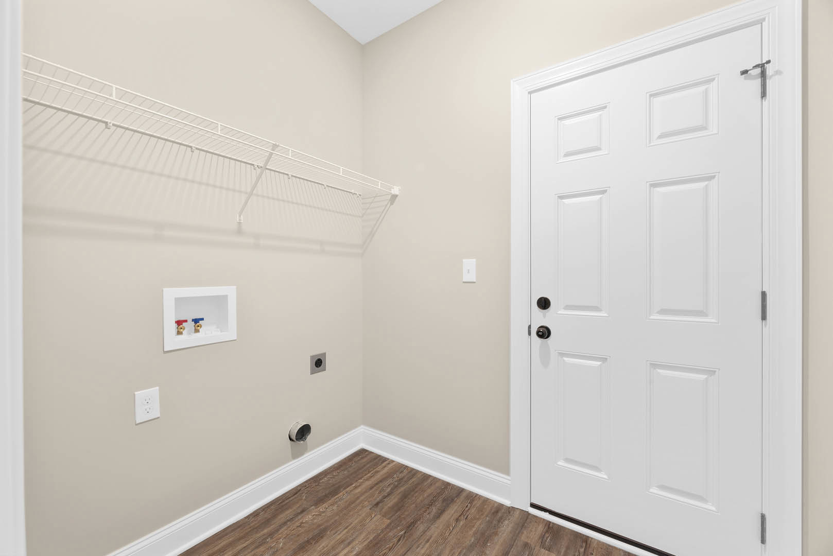 White paneled door with black knob, white wall outlet, built-in white shelf, white box with red and blue valve, light-colored flooring, smooth plaster walls, and ceiling.
