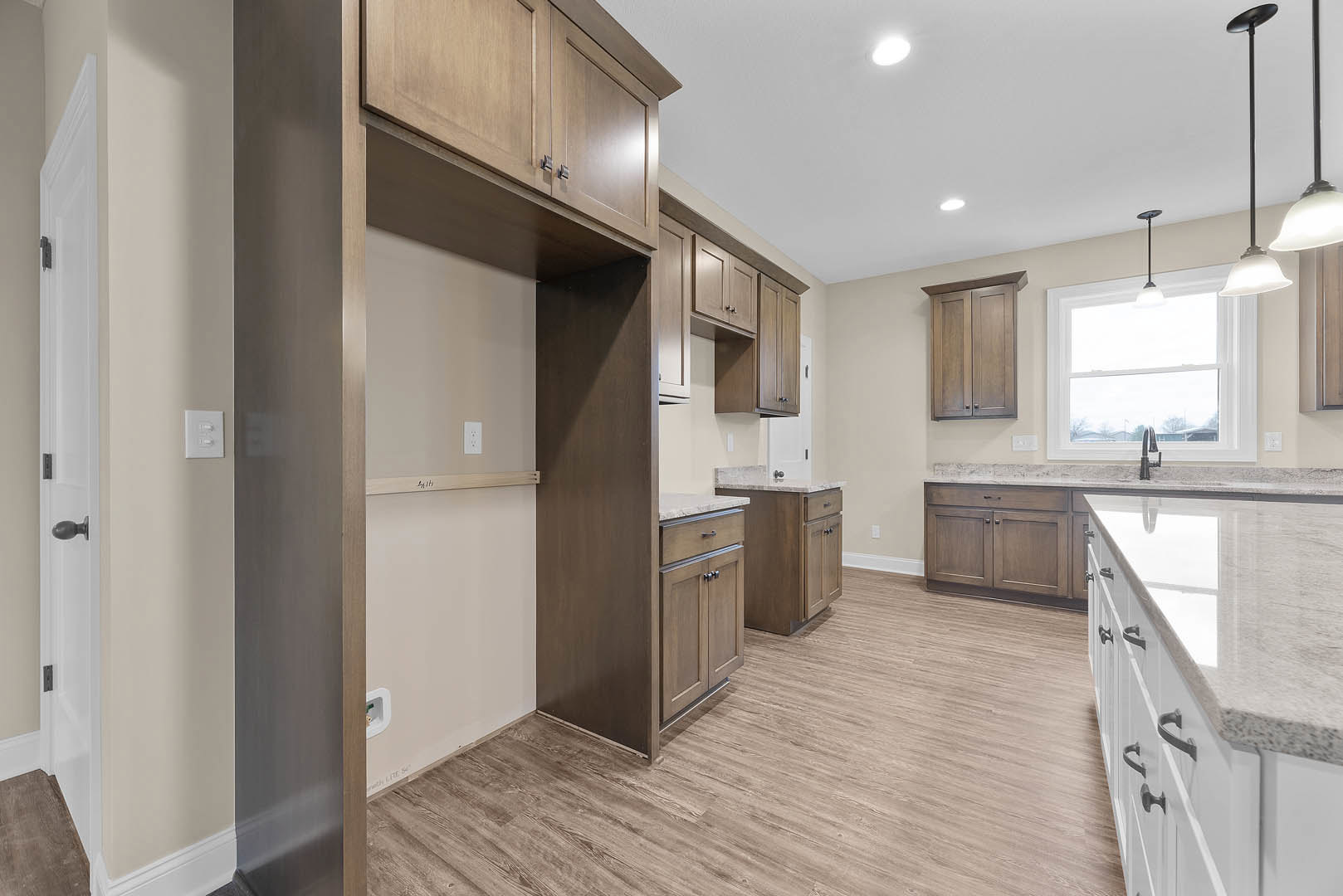 Kitchen with natural wood cabinets, matching wood floor, white ceiling with recessed lights, window with white frame, open shelving, and white light switch with knobs