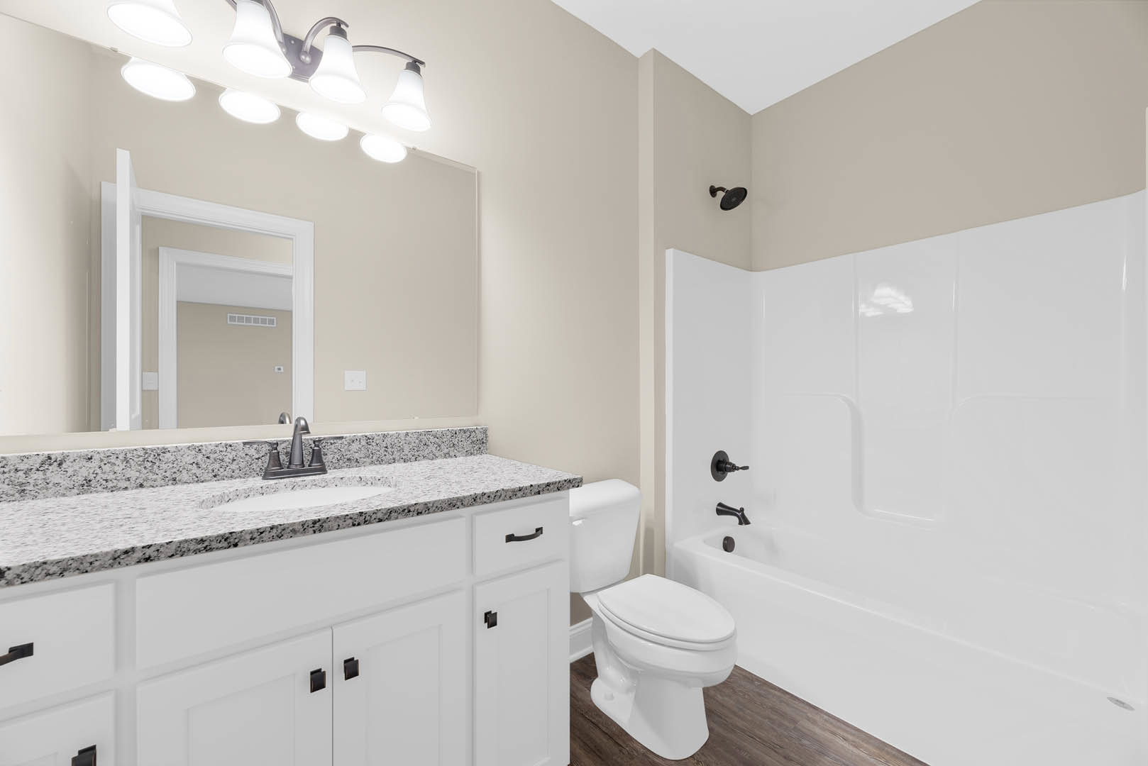 White bathroom with ceramic tile floor, undermount sink set in stone countertop, modern faucet, closed toilet, and white bathtub against tiled wall
