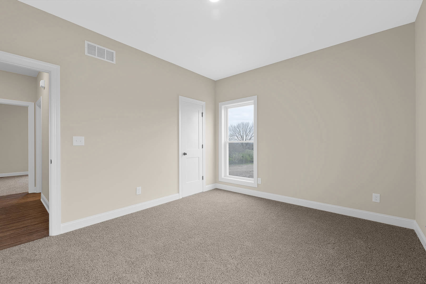 Carpeted room featuring a white door with black knob, window overlooking a tree, white walls with molding, and wood laminate flooring near the entrance.