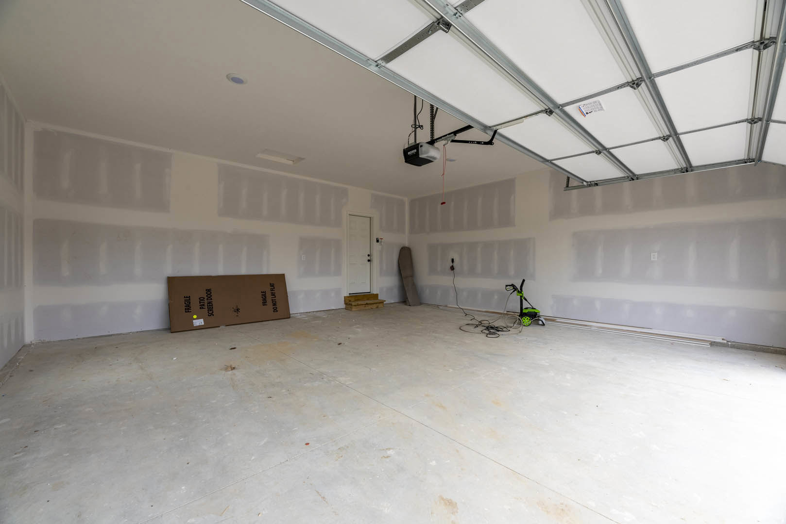 Garage with smooth white plaster walls, white ceiling, white door with black knobs, bicycle leaning against wall, brown box with black text, exposed wires, and security camera