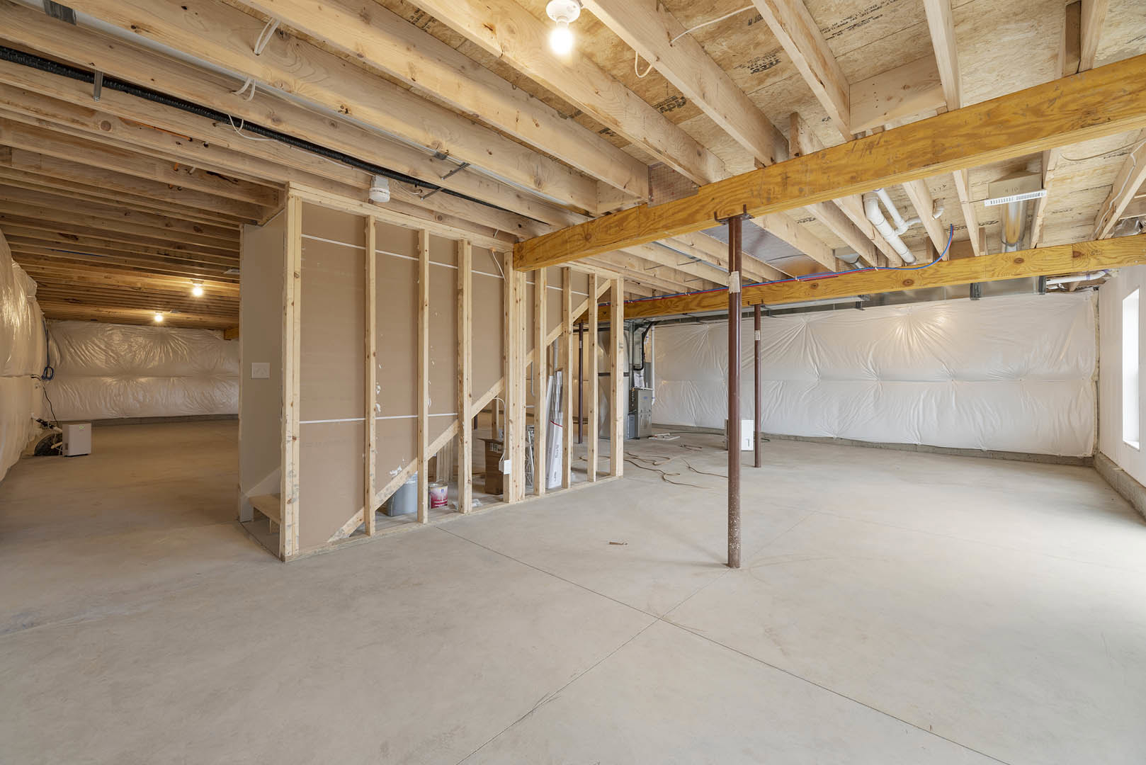 Wooden ceiling with exposed beam, concrete floor, metal support pole, white electrical box with green indicator light, unfinished walls, visible pipes and insulation, person