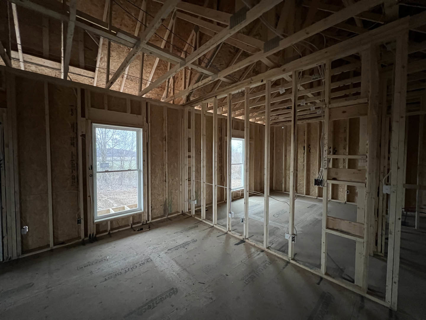 Open room with exposed wood ceiling beams, large windows framed in white, concrete floor, and views of green trees outside