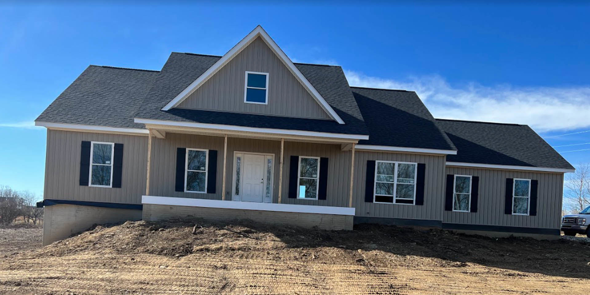 Partially built house on a hill with white siding, glass-paneled door, white-framed windows, and blue sky overhead