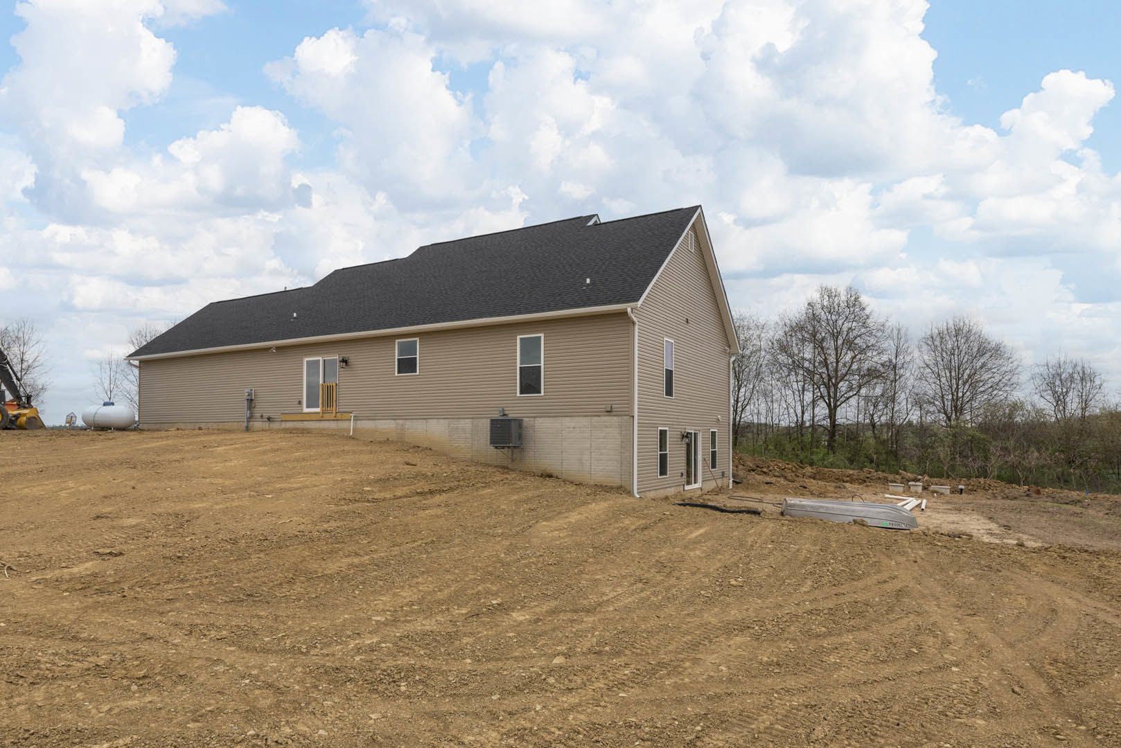 Partially built house with exposed framing, surrounded by a dirt field, under a blue sky with scattered clouds