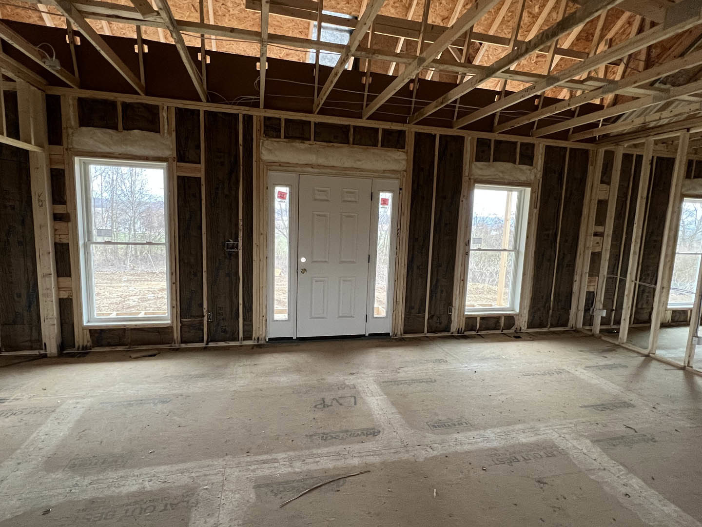 Concrete floor with white lines, white door flanked by two windows, wooden ceiling beams, large window with white frame showing trees outside