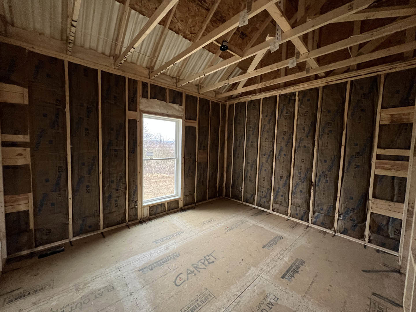 Living room with exposed wood ceiling beams, wide-plank hardwood floor, and large window framed in white trim.