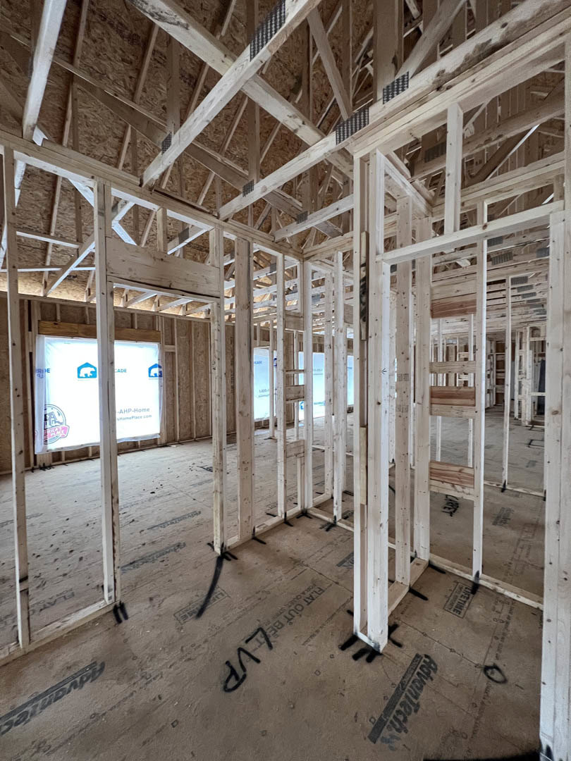 Exposed wood framing with ceiling beams, unfinished floor, and partially installed window in a residential interior under construction