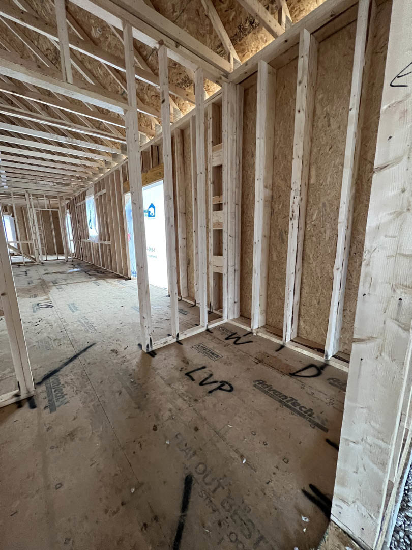 Exposed wood framing and beams in an unfinished room with a window, construction materials visible on walls and ceiling