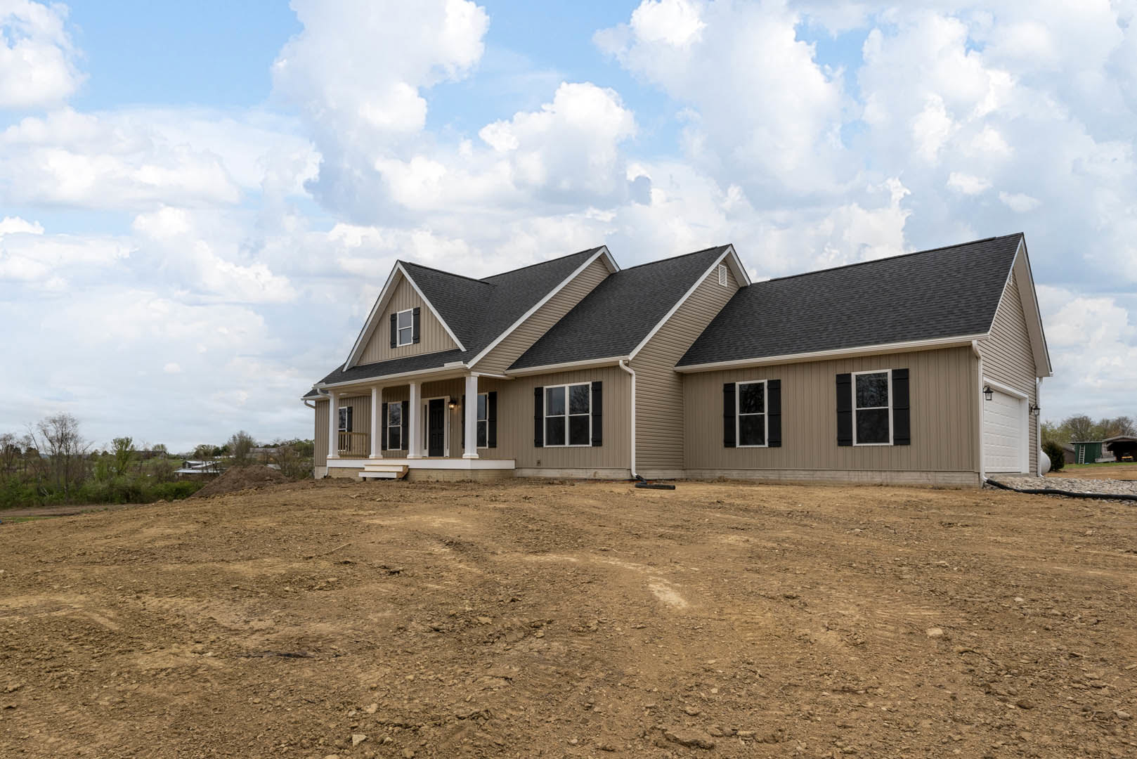 White custom home with black shuttered windows, white trim, and a dirt yard under a cloudy sky