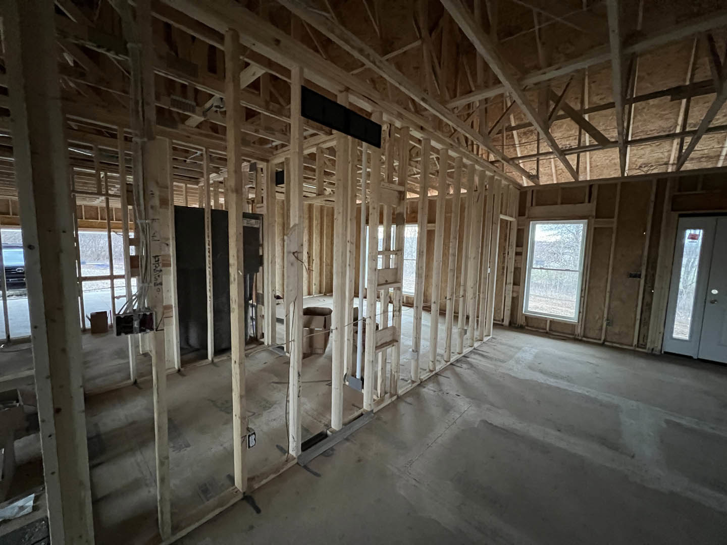 Living room with exposed wood ceiling beams, large window framed in wood, black rectangular wall sign, and wooden door.