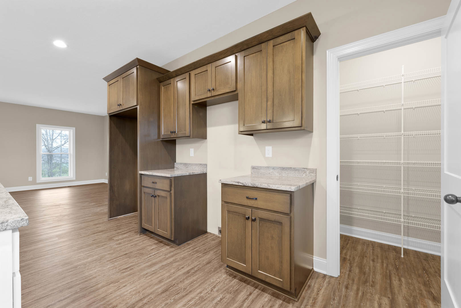 Modern kitchen with white shaker cabinets, marble countertops, stainless steel appliances, large window overlooking trees, and a central island with matching marble top