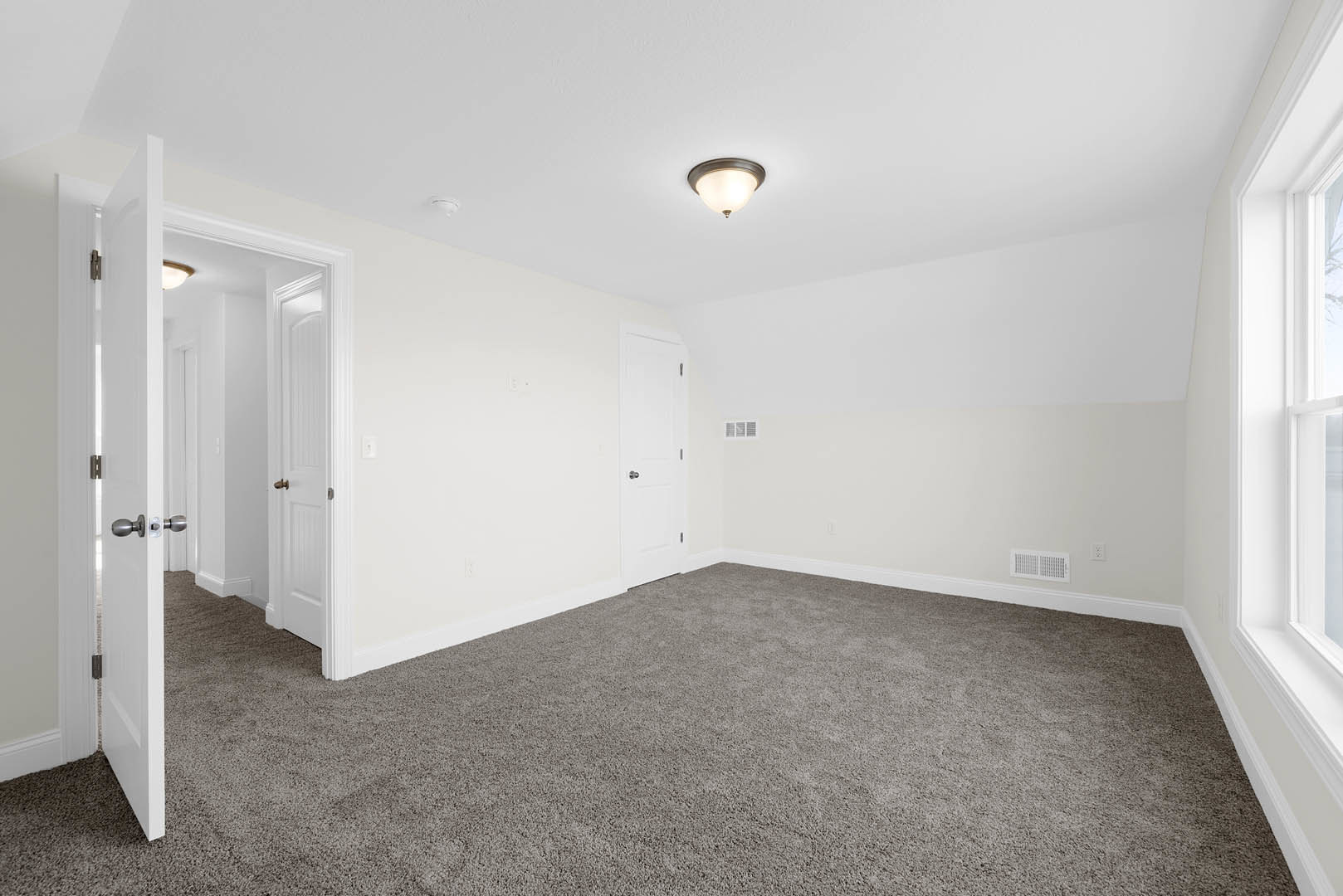 Carpeted room with white walls, ceiling-mounted light fixture, and white door featuring a silver doorknob