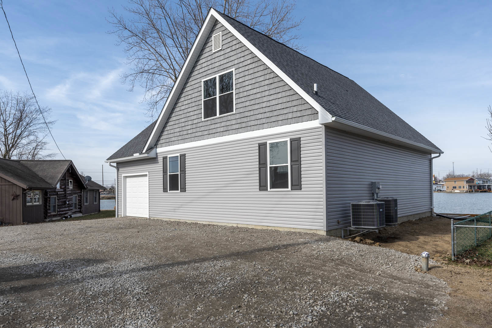 Two-story home with attached garage, parked car in driveway, white siding, gravel driveway, white-framed windows, chain link fence, and Rockingham Meeting House visible in the