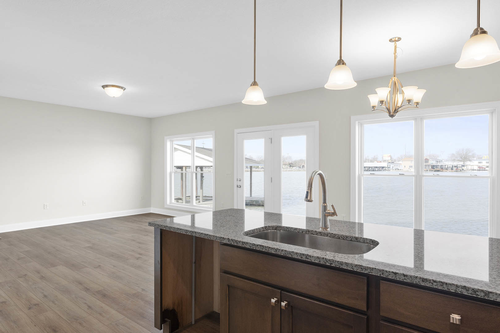 Spacious kitchen featuring a large central island with stone countertop, wide window overlooking water, modern cabinetry, stainless steel sink with sleek tap, and contemporary