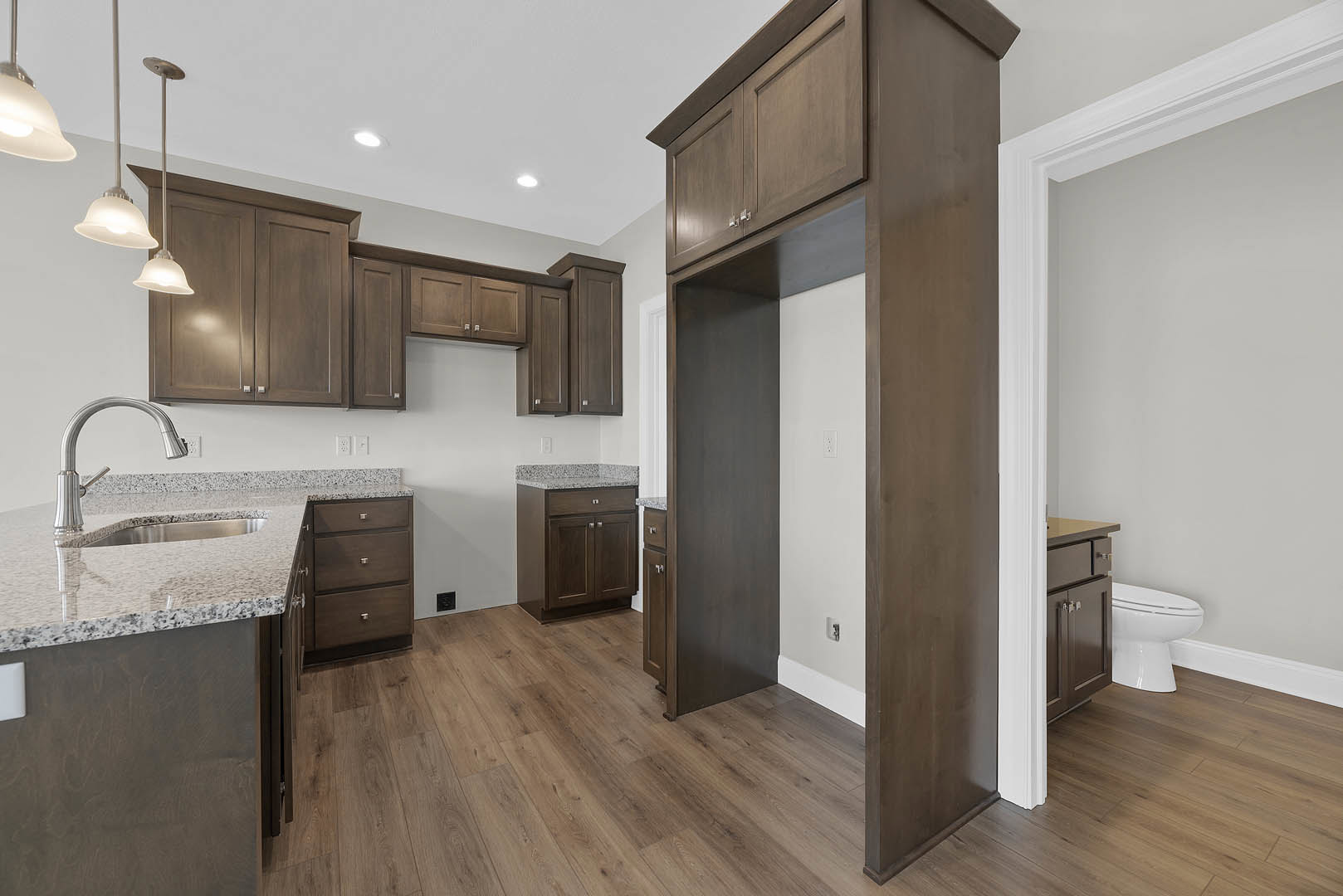 Kitchen featuring dark wood cabinetry, marble countertops, tile flooring, stainless steel sink, and modern light fixture