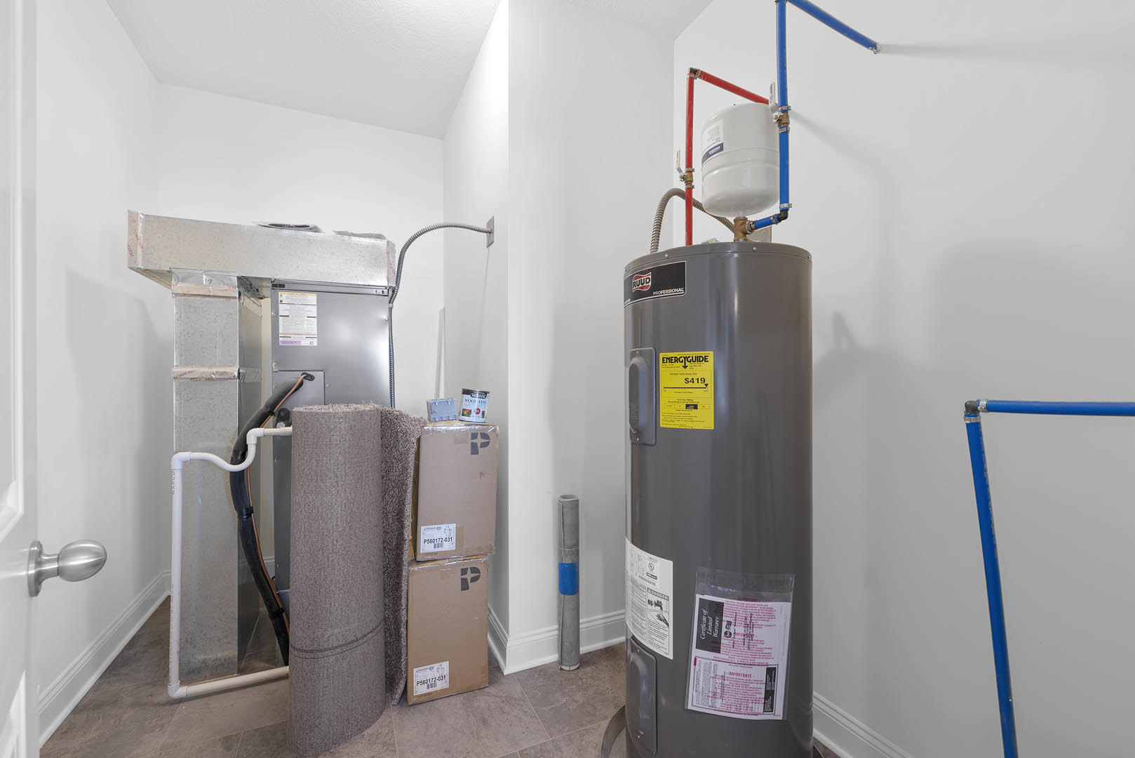 Large grey cylindrical tank with blue pipes mounted against a white wall, yellow label and sign visible, surrounded by containers and fabric rolls.