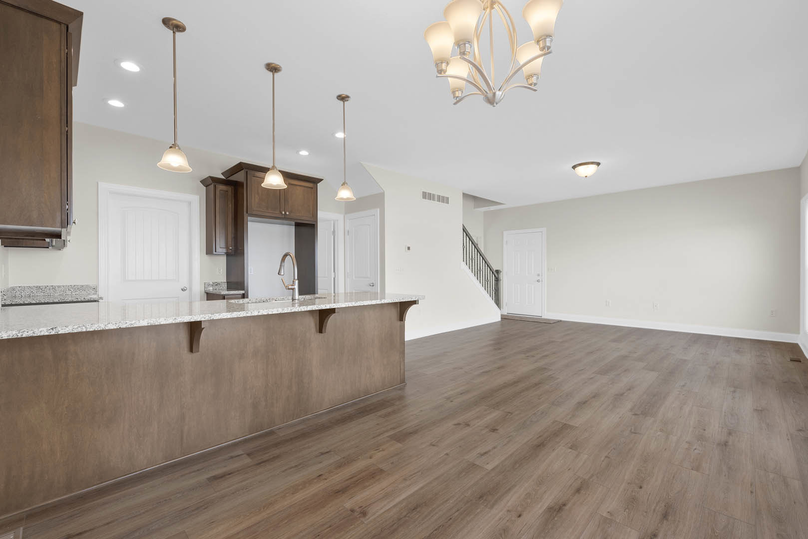 Open-concept kitchen and living room featuring wood flooring, white cabinetry, stone countertop, modern chandelier, and white doors with silver hardware