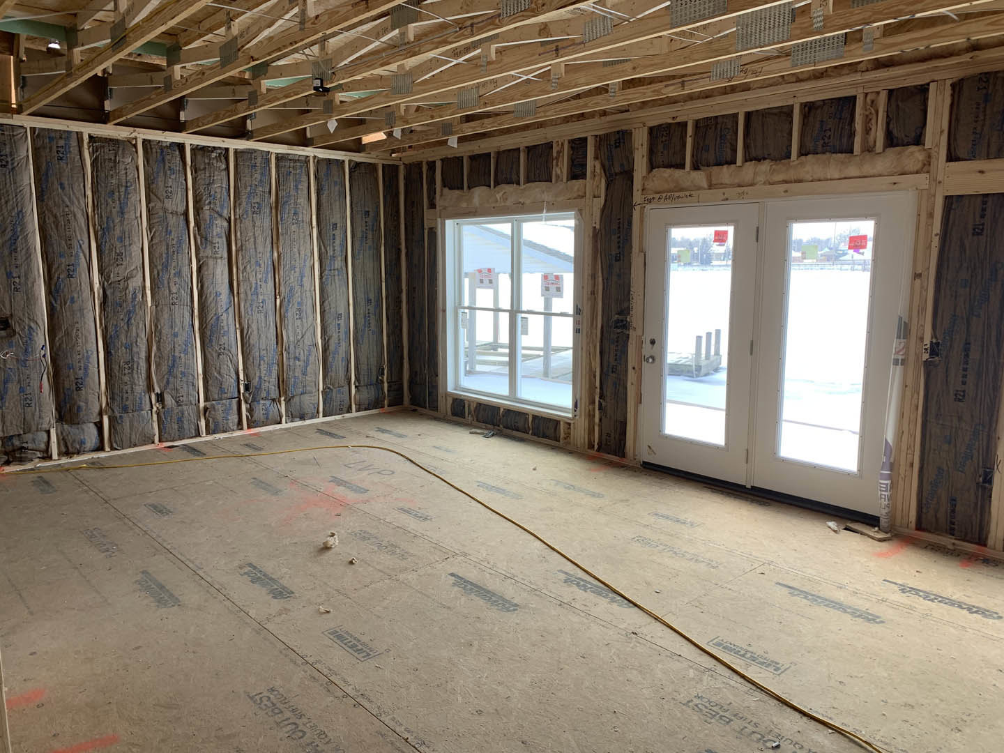Double glass doors framed by wood beams, ceiling with exposed roof truss, wall lined with insulation, yellow electrical cable visible along unfinished interior.