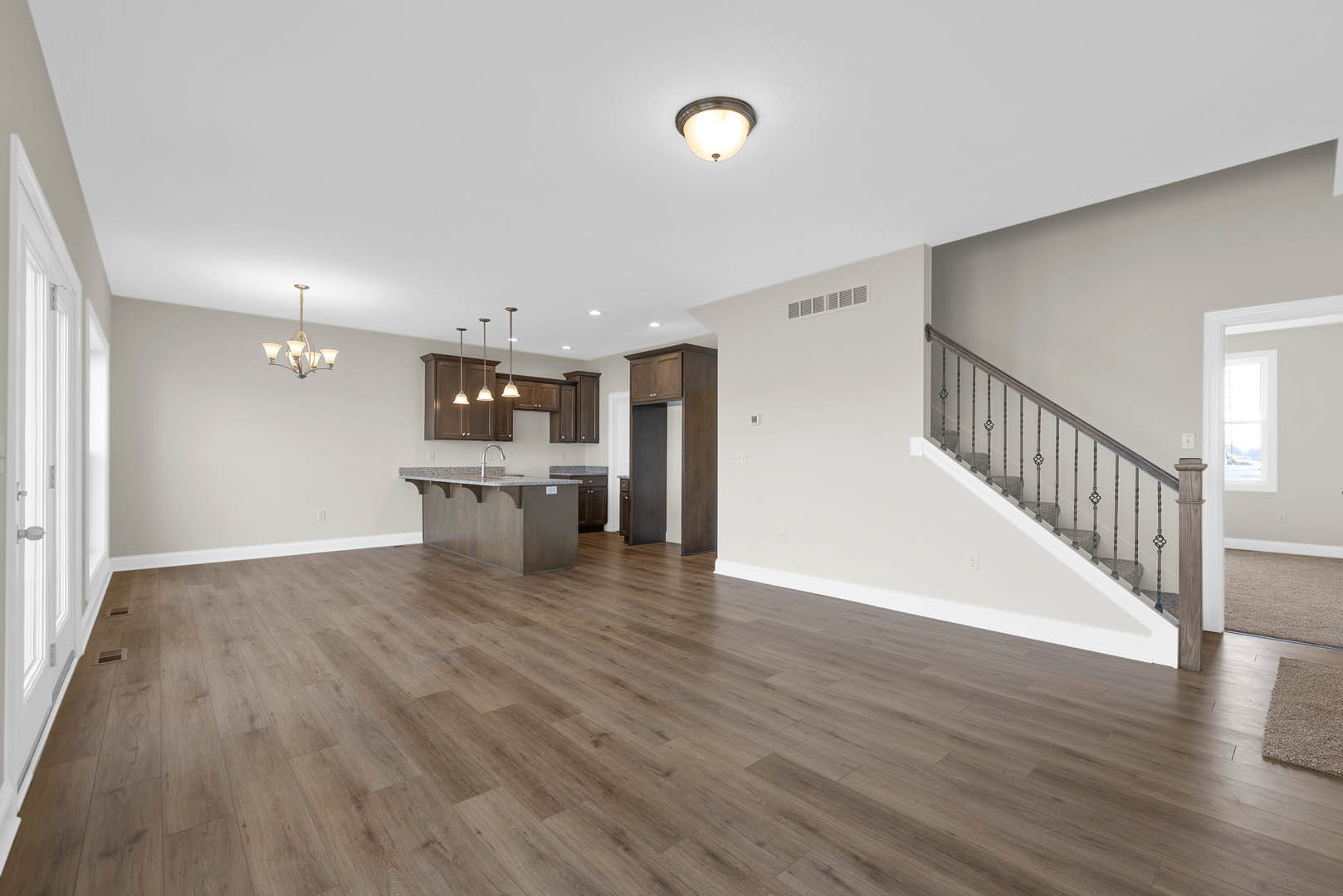 Open-concept room featuring wood flooring, marble kitchen countertops, white cabinetry, and a staircase with wooden treads; modern chandelier and recessed ceiling lights illuminate
