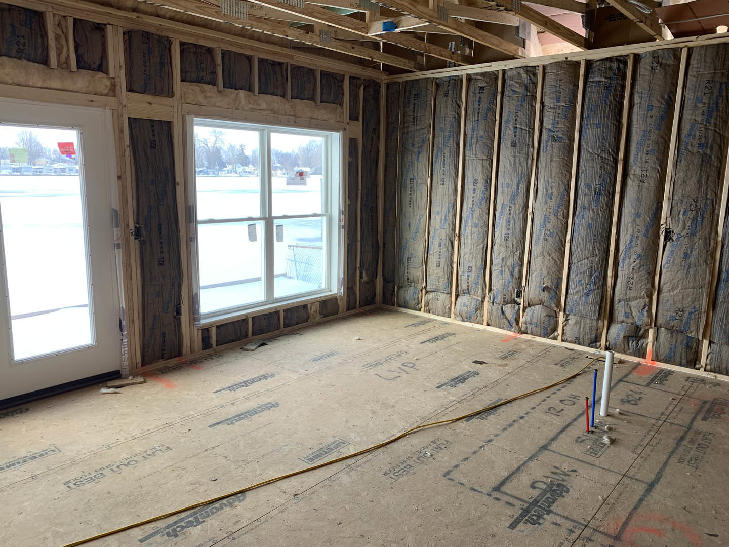 Room with wood-paneled wall, large window letting in bright light, yellow cable on floor, black bags against wall, shadow of sign cast on ground