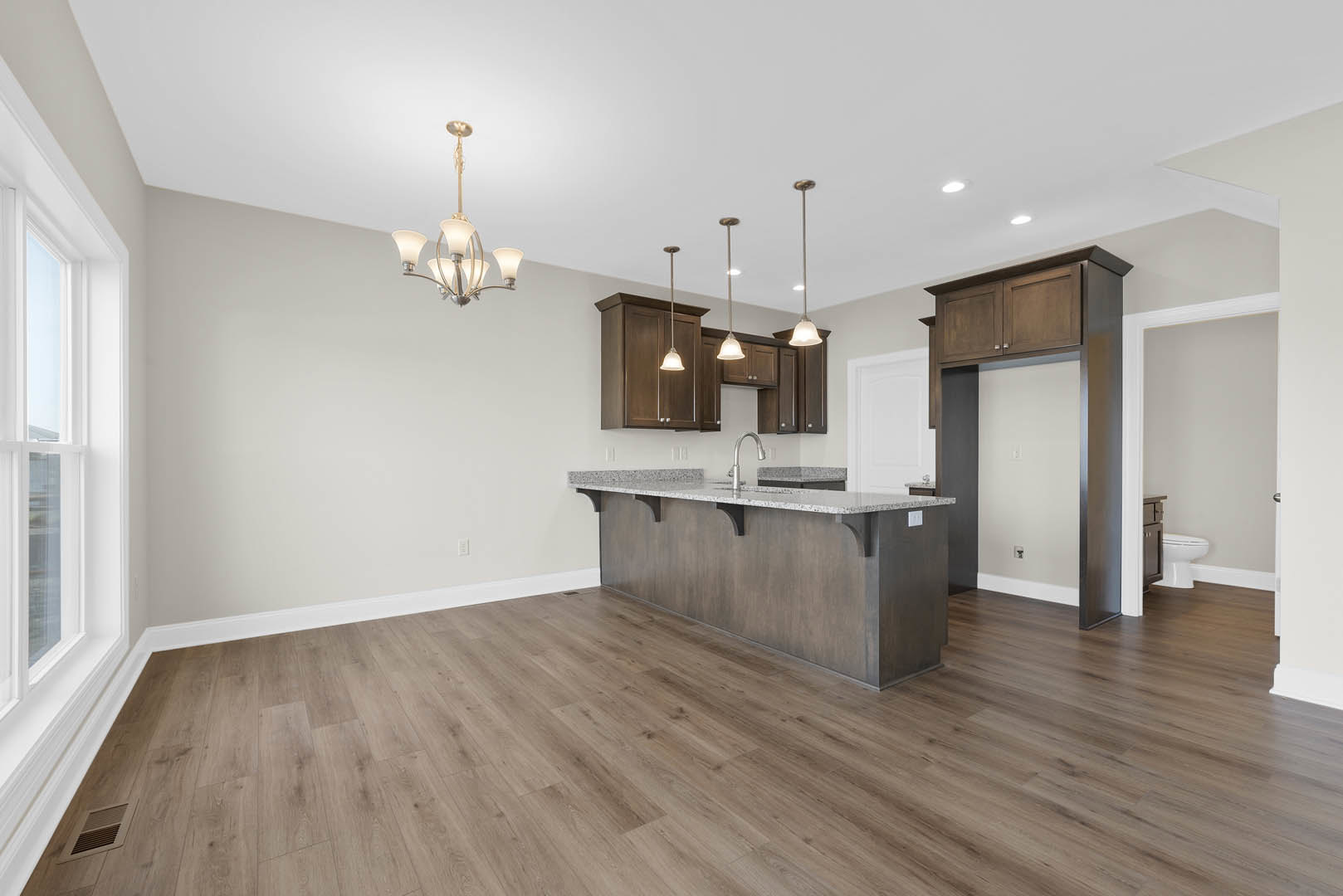 Kitchen with wide plank wood flooring, marble countertop, white cabinetry, and modern chandelier; partial view of adjacent bathroom with white toilet.