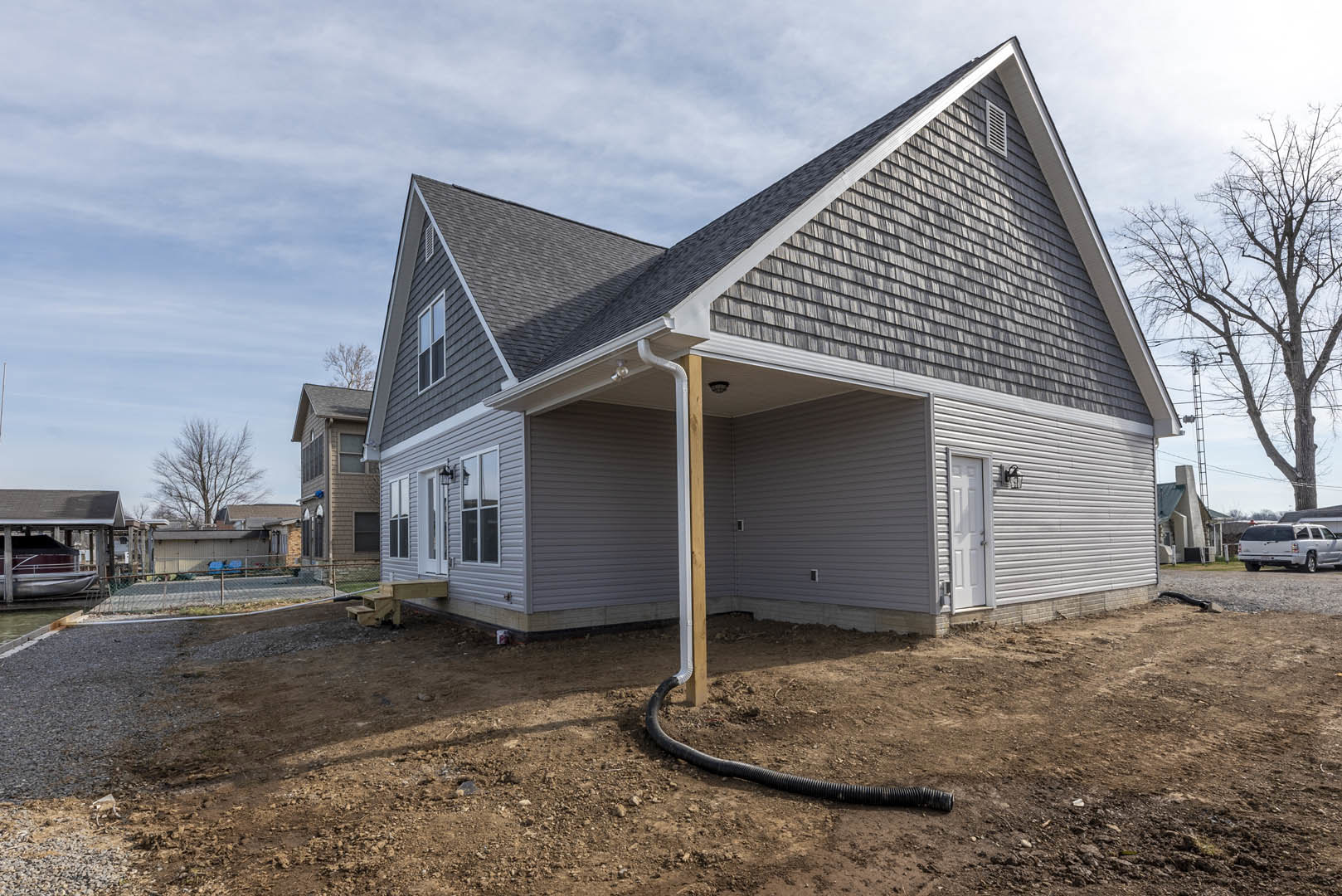 Two-story house with gray siding, shingled roof, white front door, large windows, and a metal pipe extending from a pole in the front yard; leafless tree and white truck parked