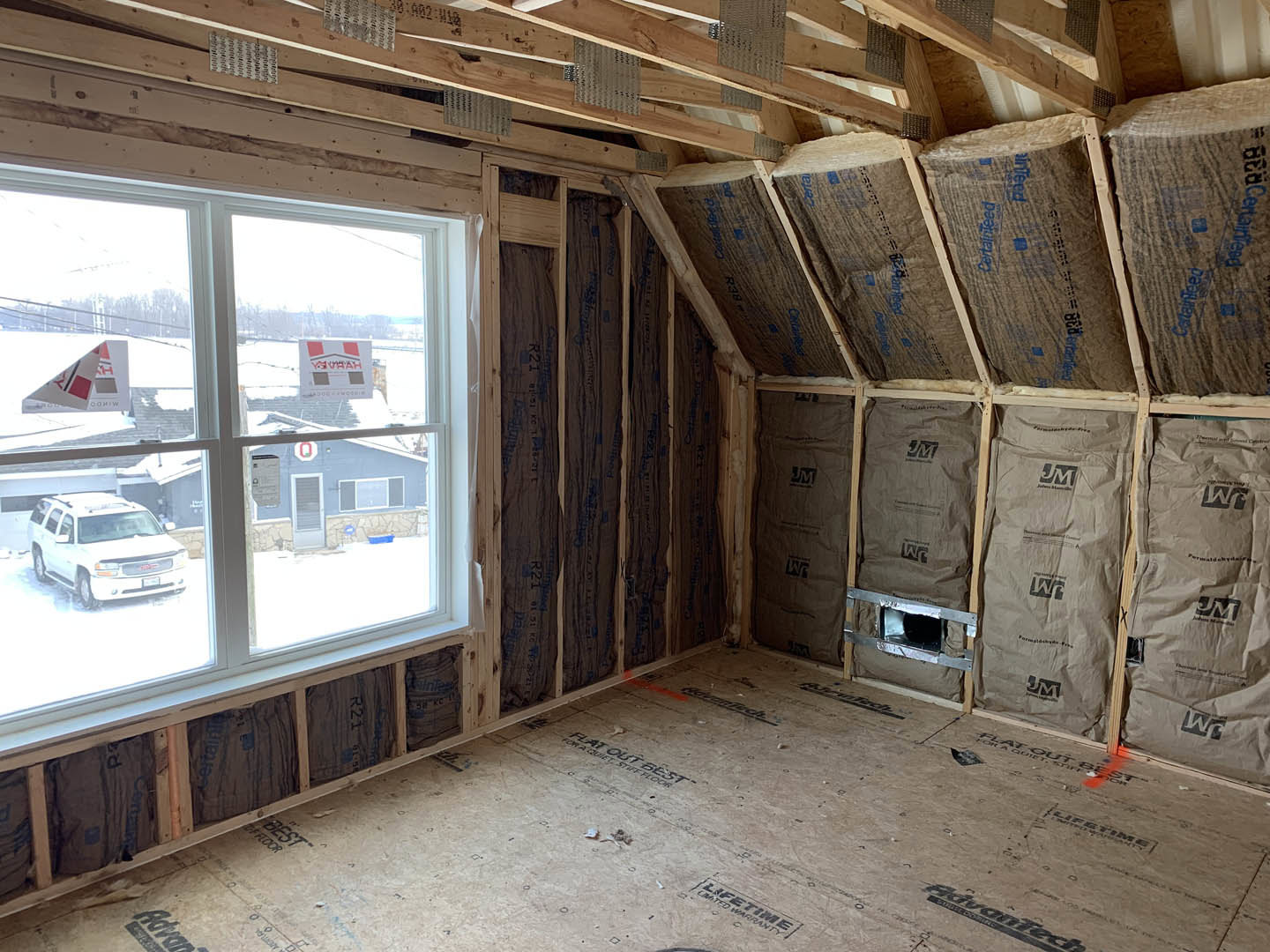 Unfinished room with exposed wooden ceiling beams, wall insulation, and two windows letting in natural light