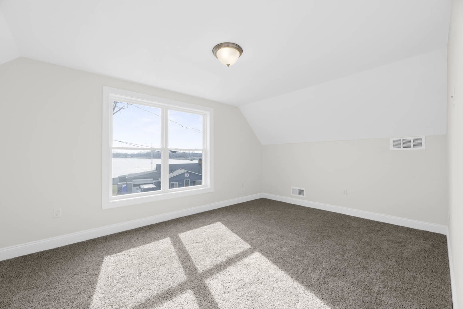 Carpeted room with white walls, large window overlooking river and snowy city, ceiling light fixture with frosted shade, floor vent near window.