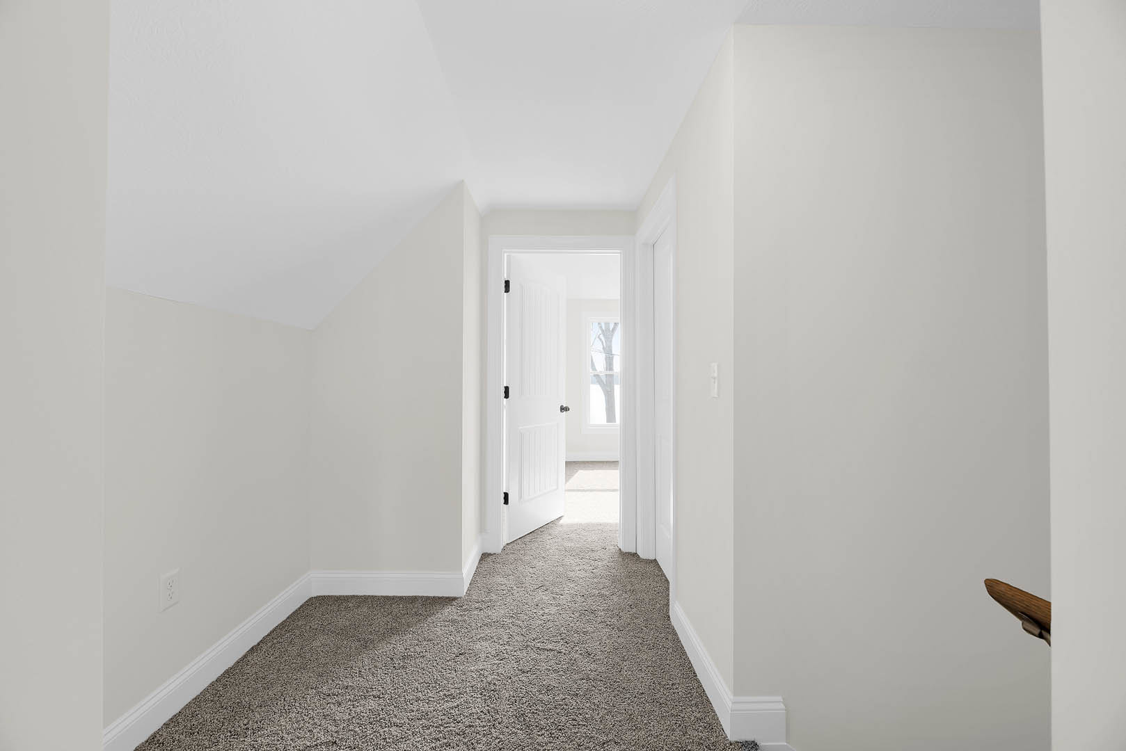 White hallway with carpeted floor and white trim, open white door with black handles and window, white walls and ceiling